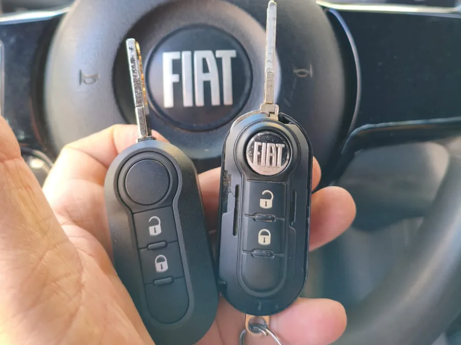 Chave canivete e telecomando Fiat prontos, na mão, com o volante do carro atrás